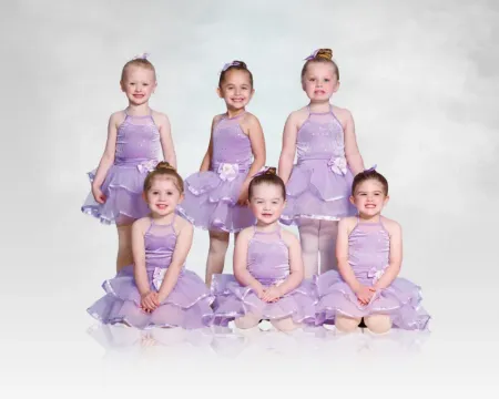 Six young dancers in lavender tutus posing in two rows against a white background