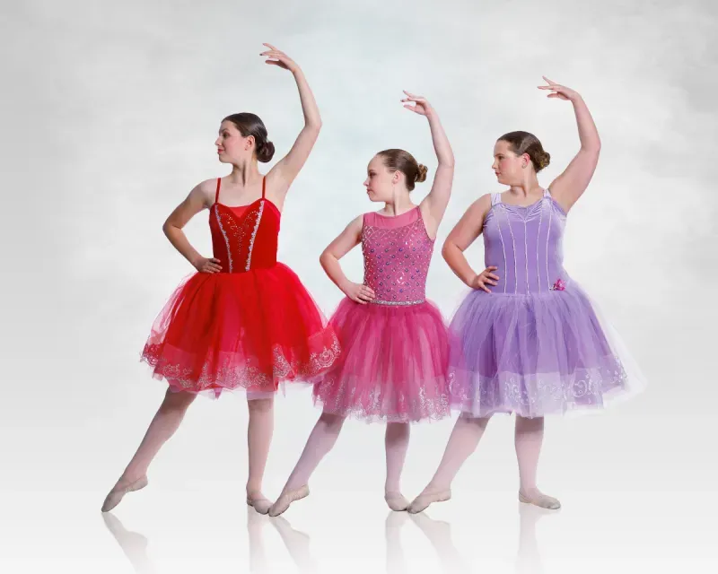 Three ballet dancers in red, pink, and lavender tutus pose with raised arms against a white background
