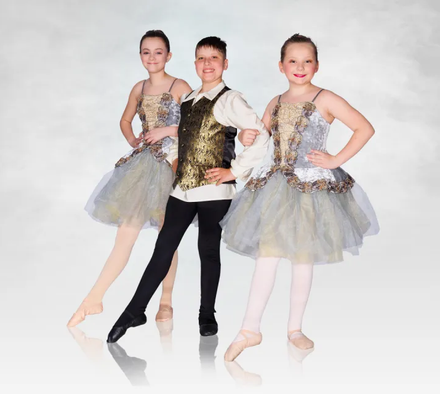 Three ballet dancers posing in sparkly silver and gold costumes on a white studio backdrop