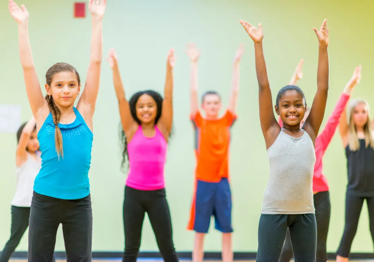Children in workout clothes stretching with arms raised in a dance class