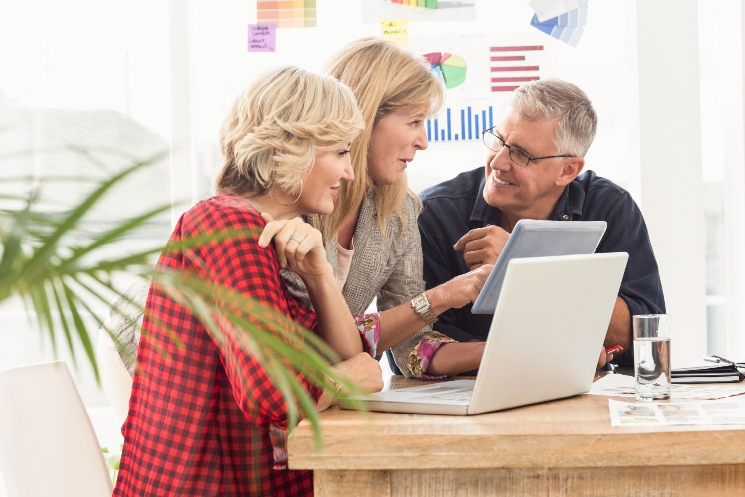 Three coworkers collaborating around a laptop at a desk in a bright office