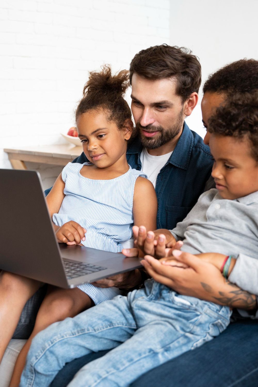 Adult and two children using a laptop on a couch, focused on the screen