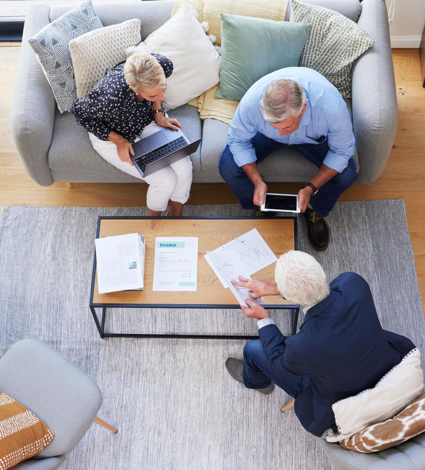 Three people seated around a coffee table reviewing papers and a tablet in a living room