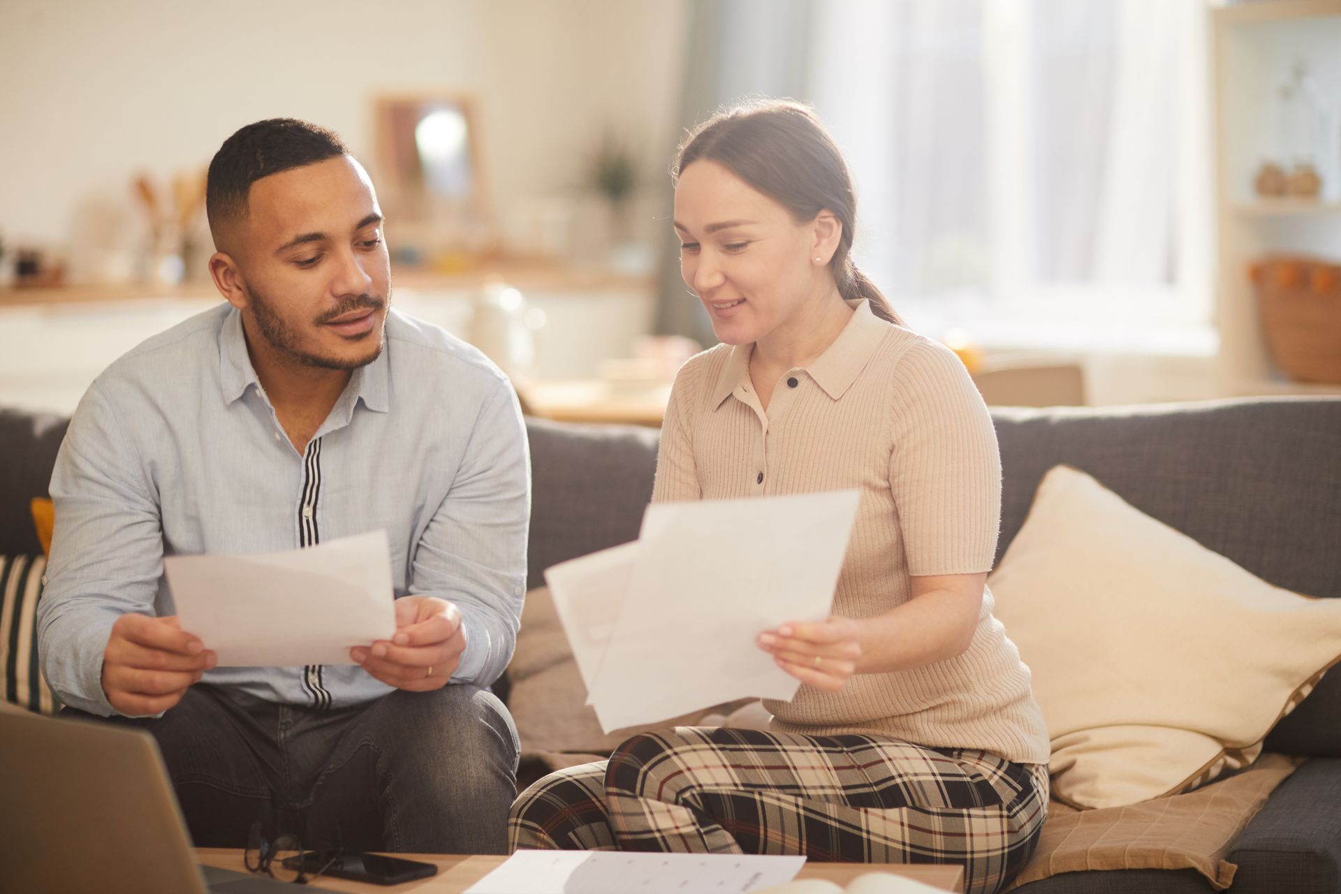 Two people sitting on a couch reviewing papers in a bright living room