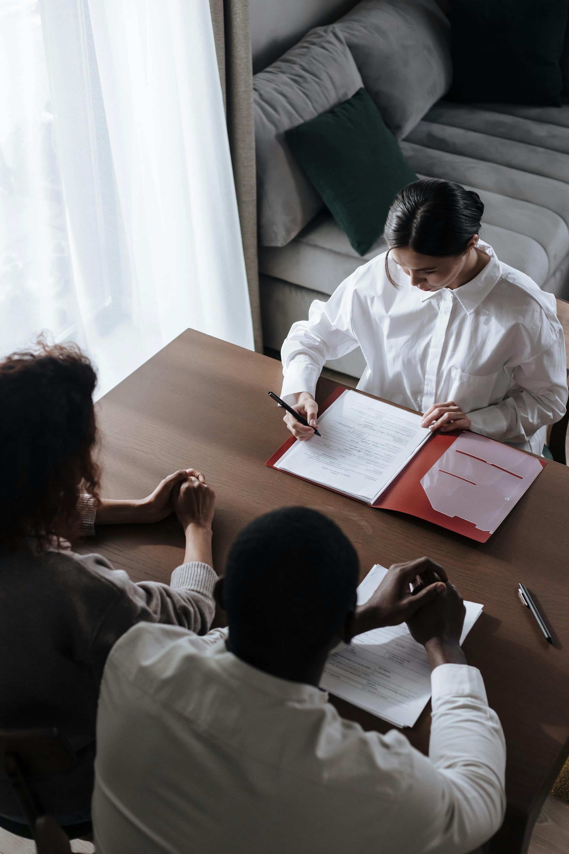 Three people sit around a table reviewing documents in a bright living room.
