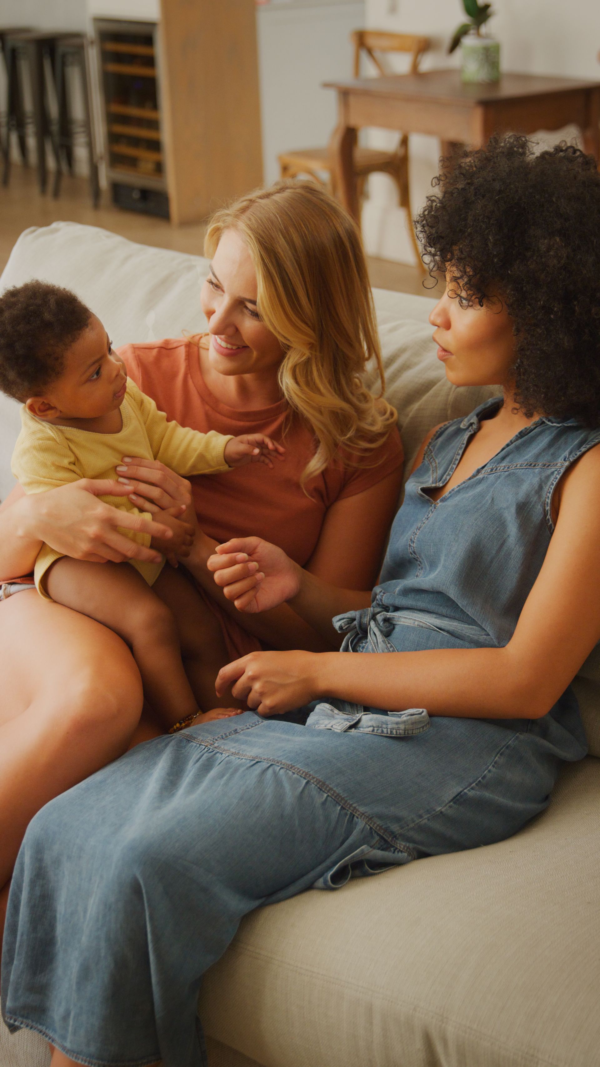 Three people sitting on a couch, smiling and holding a baby in a cozy living room.