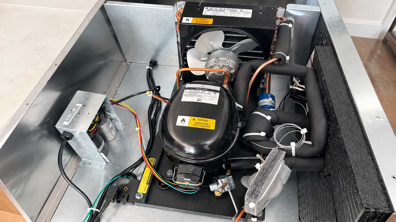 Open appliance with exposed compressor, wires, and metal components in a gray housing