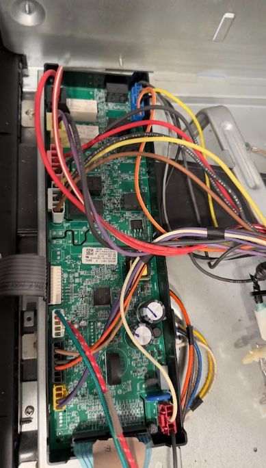 Open electronics control panel with green circuit board and tangled red, yellow, orange, and black wires