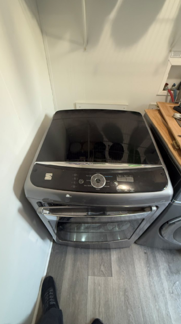 Top-loading washer in a laundry nook beside a dryer, with a wood countertop and white walls.