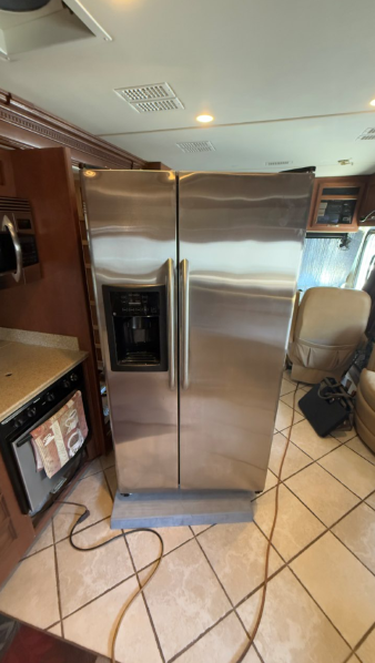 Stainless steel refrigerator in a kitchen with tan tile floor and visible cords on the floor