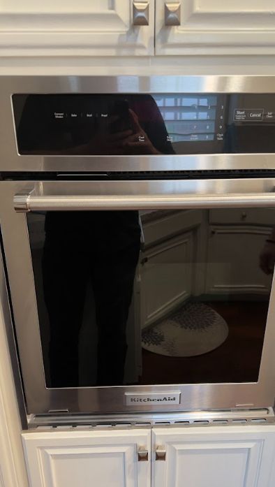 Built-in stainless steel oven with black glass door in a white kitchen cabinet wall