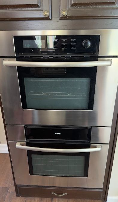 Stacked stainless steel wall oven and microwave built into dark wood kitchen cabinets.