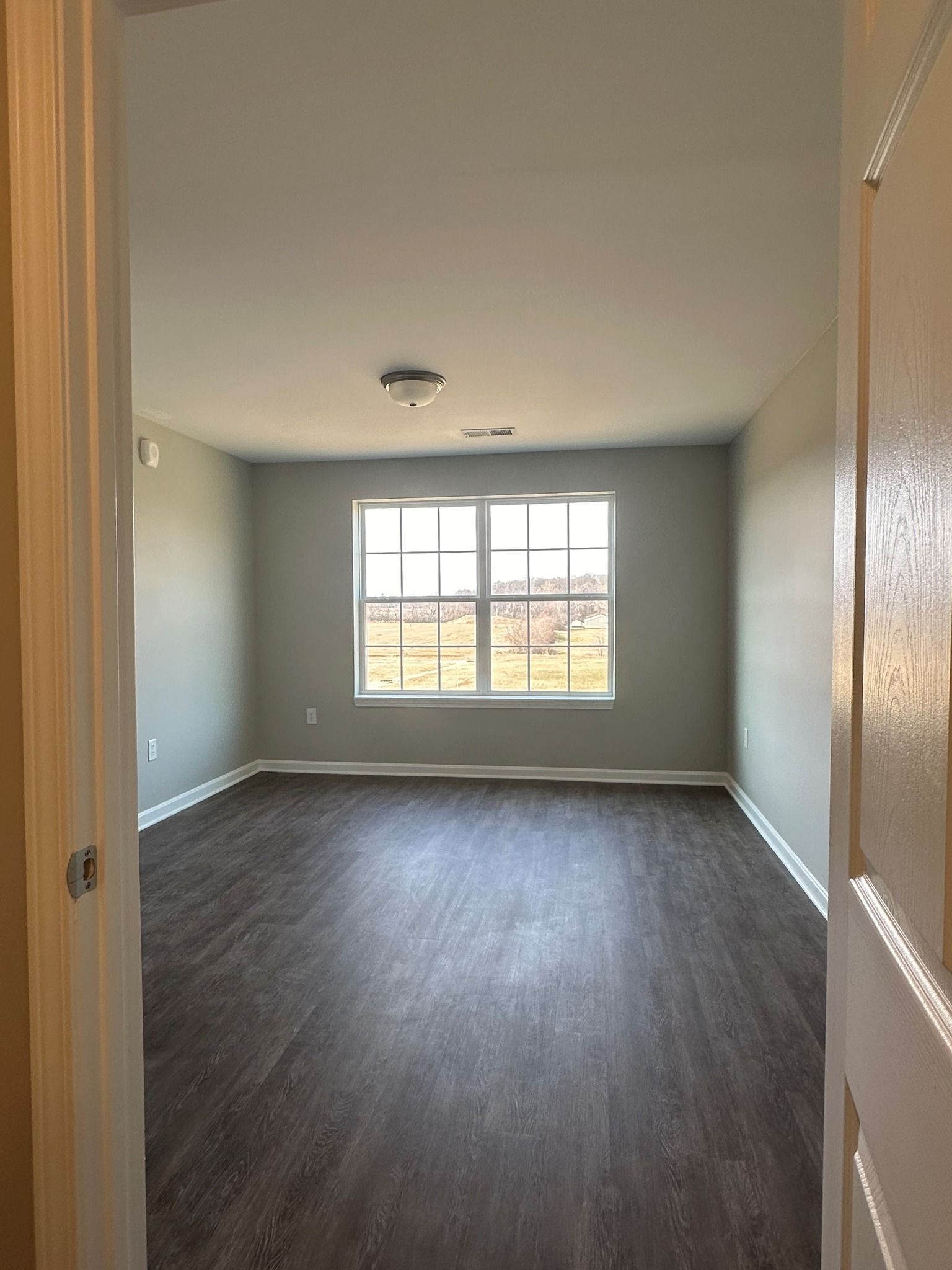 An empty living room with hardwood floors and two windows.