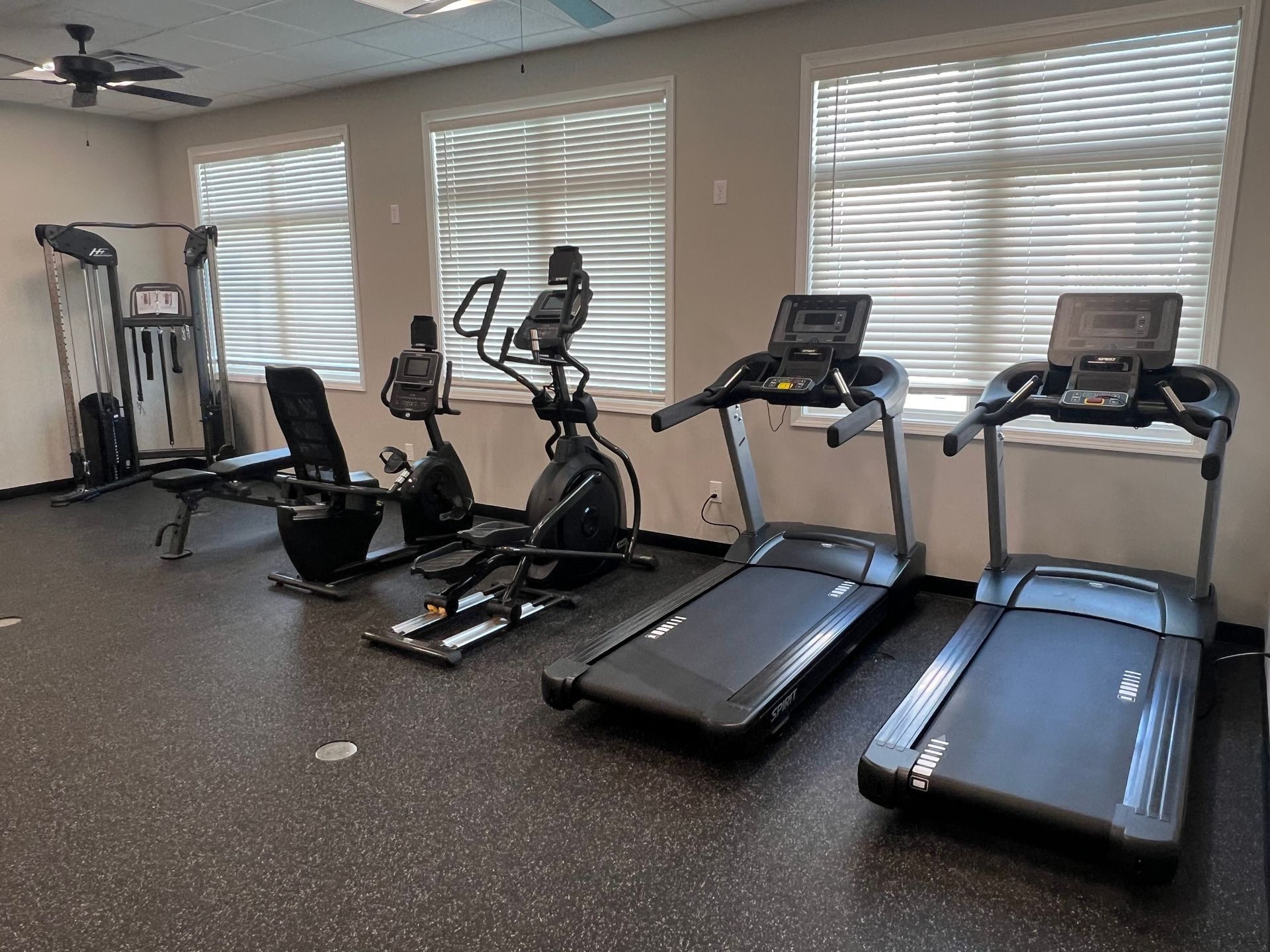 A gym with treadmills , exercise bikes , and a ceiling fan.