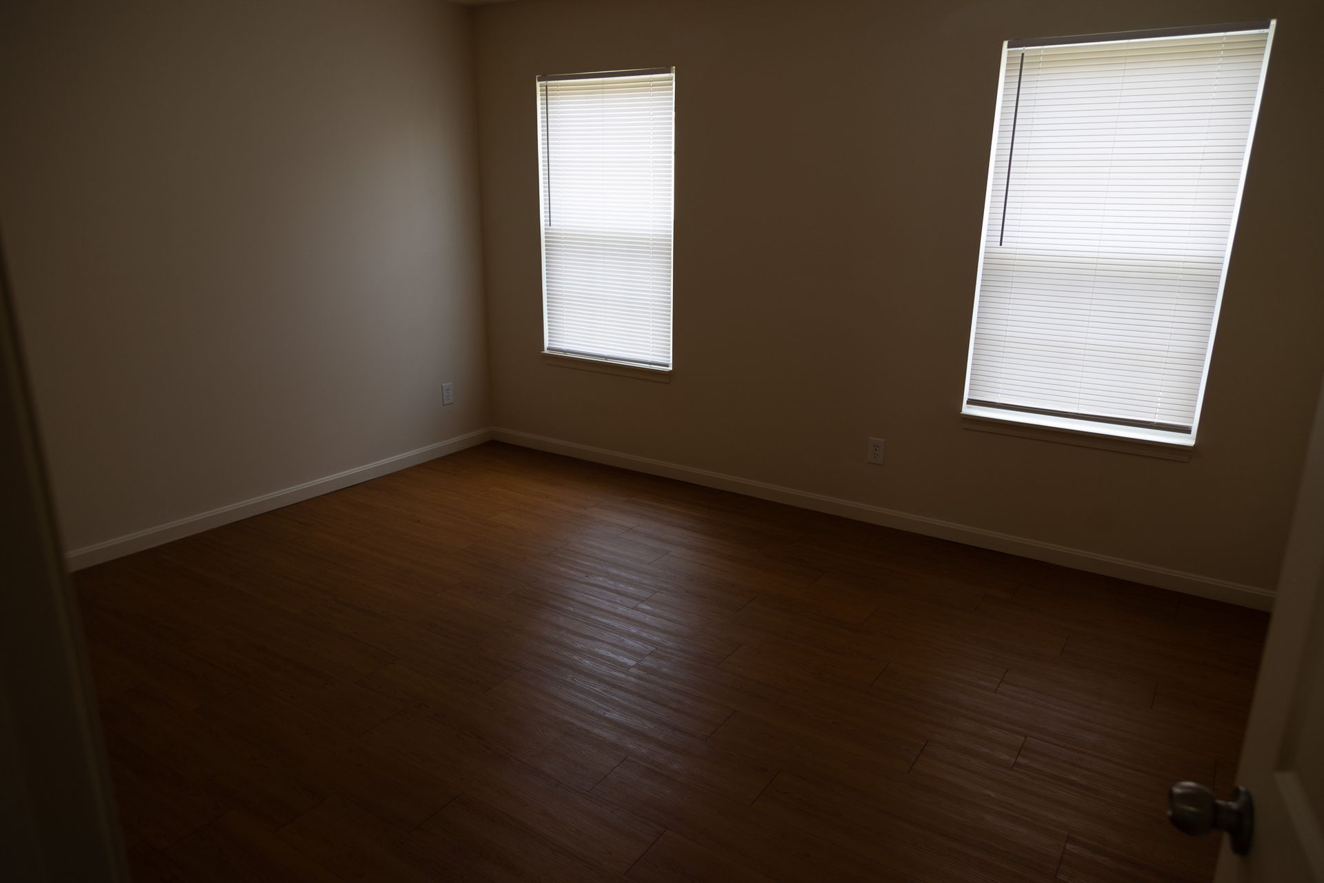An empty room with two windows and hardwood floors