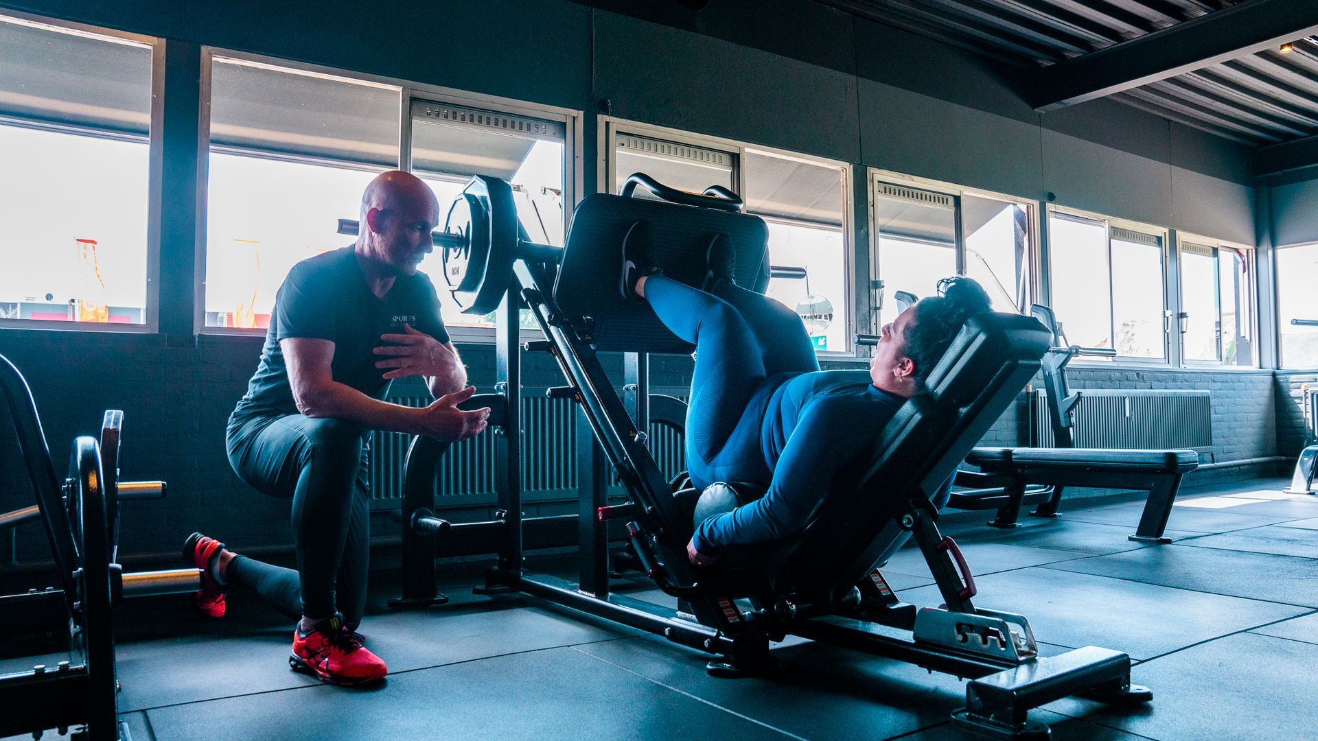 Persoon die traint op een leg press-machine in een sportschool met grote ramen.