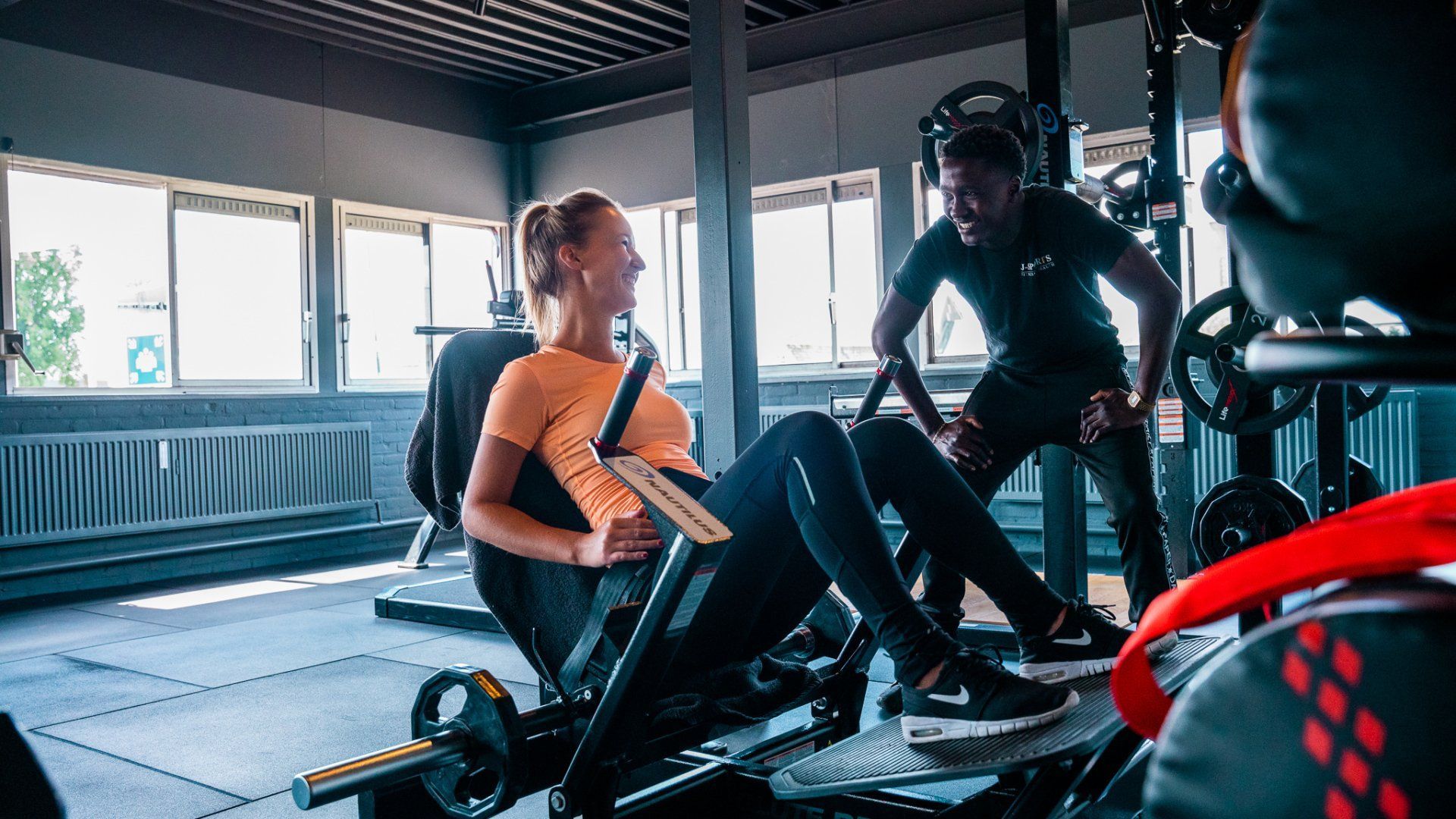 Twee mensen die trainen op roeimachines in een lichte sportschool, van wie één een oranje top draagt