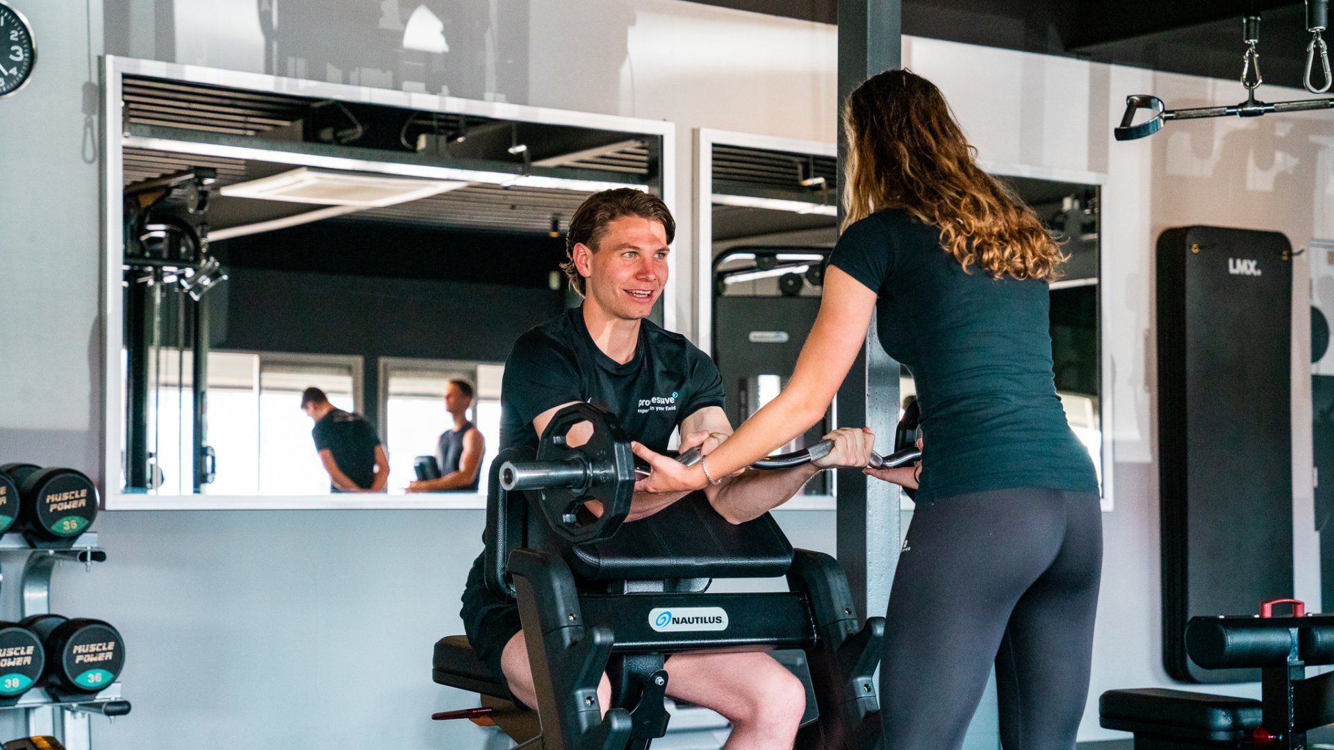 Persoon die traint op een hometrainer terwijl iemand anders coaching geeft in een lichte sportschool