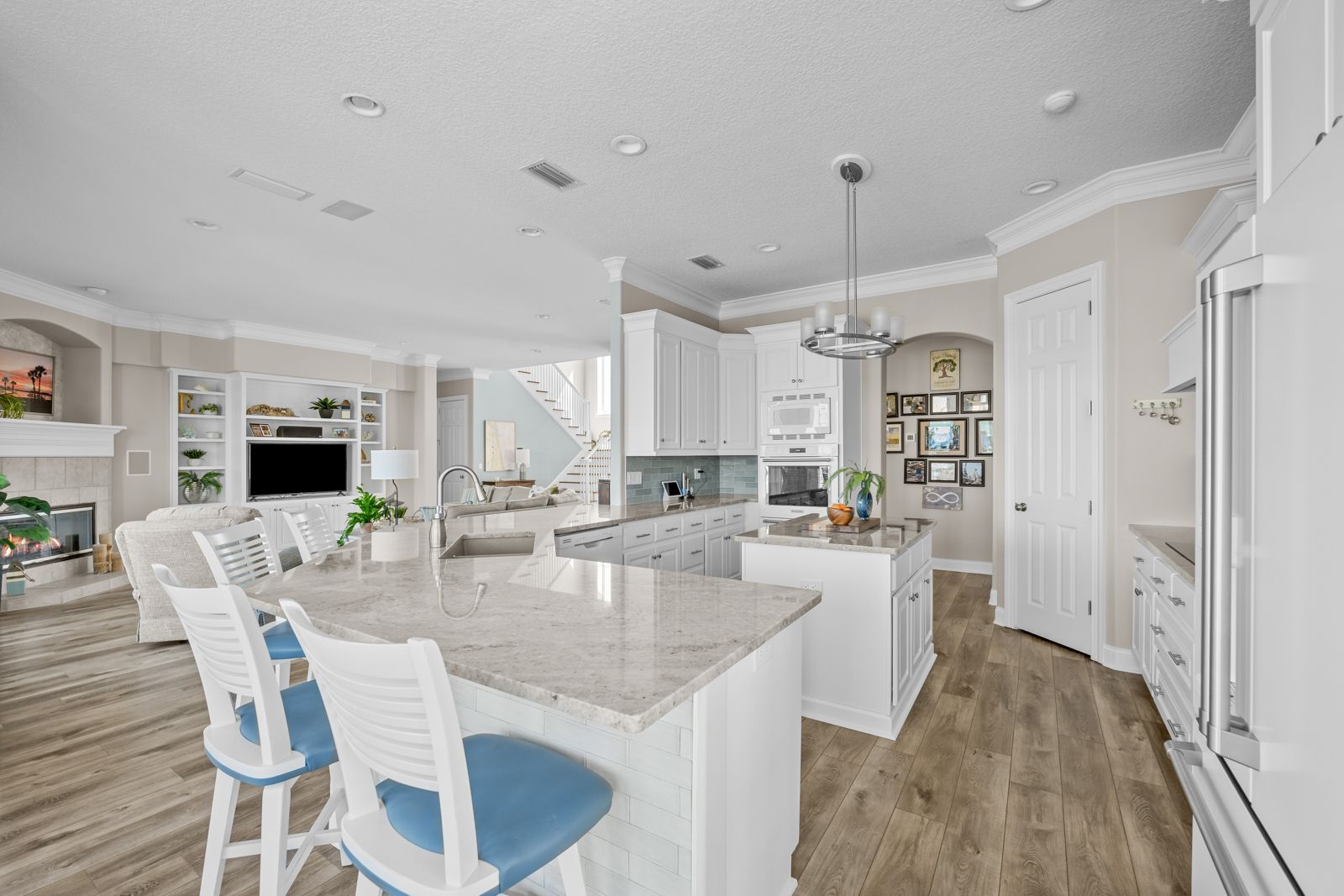 A kitchen with white cabinets , granite counter tops , stools and a large island.