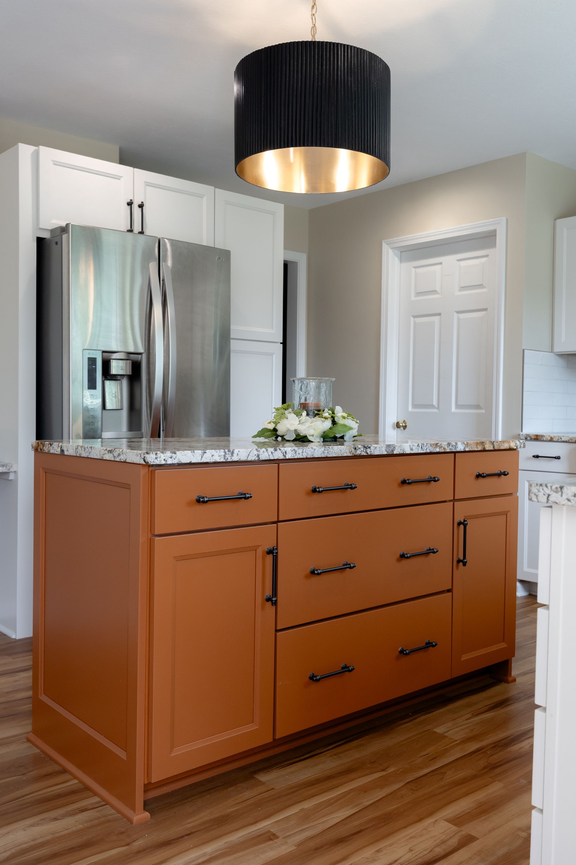 A kitchen with white cabinets , stainless steel appliances , with an orange island.