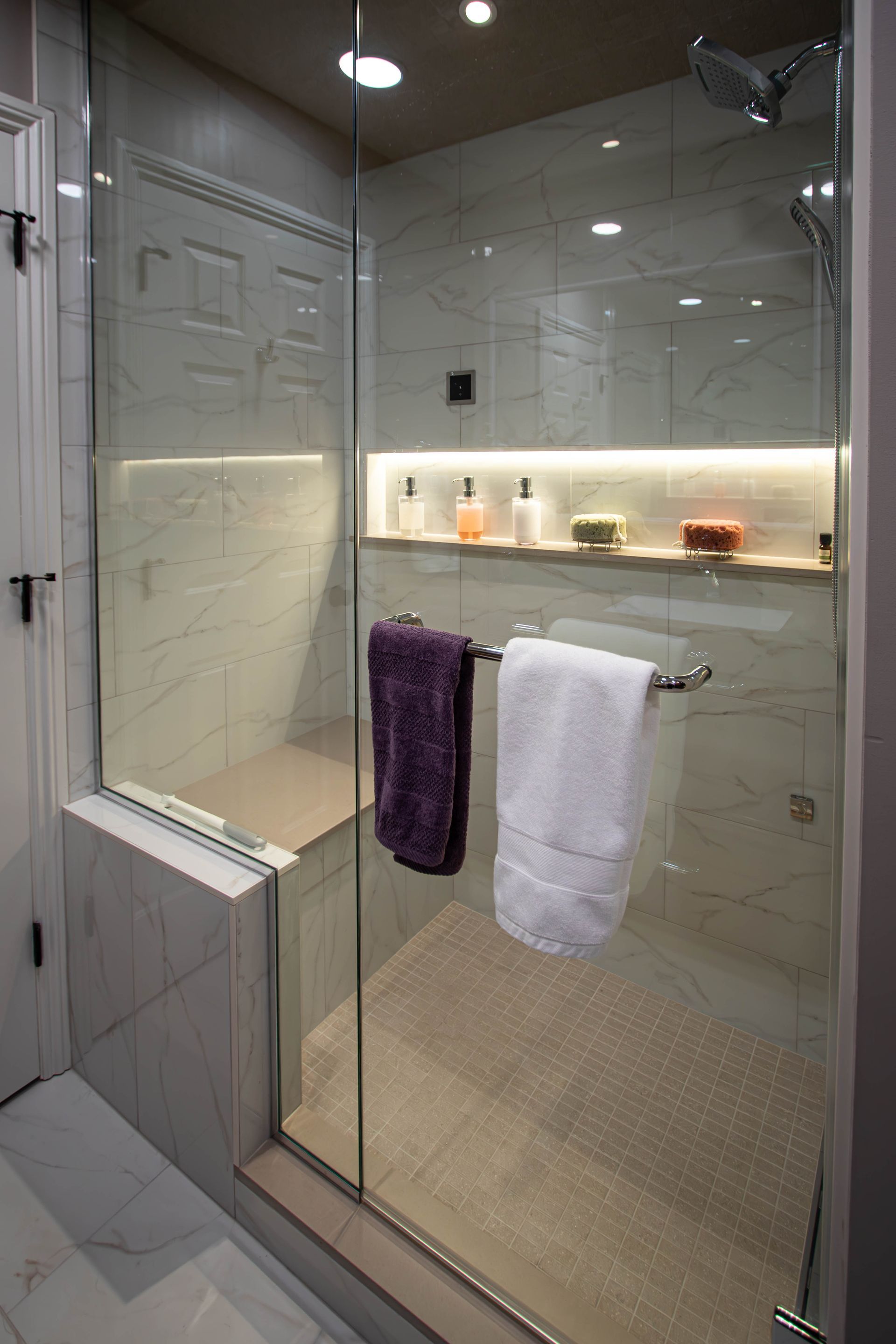 A bathroom with a walk in shower with a glass door and a bench.