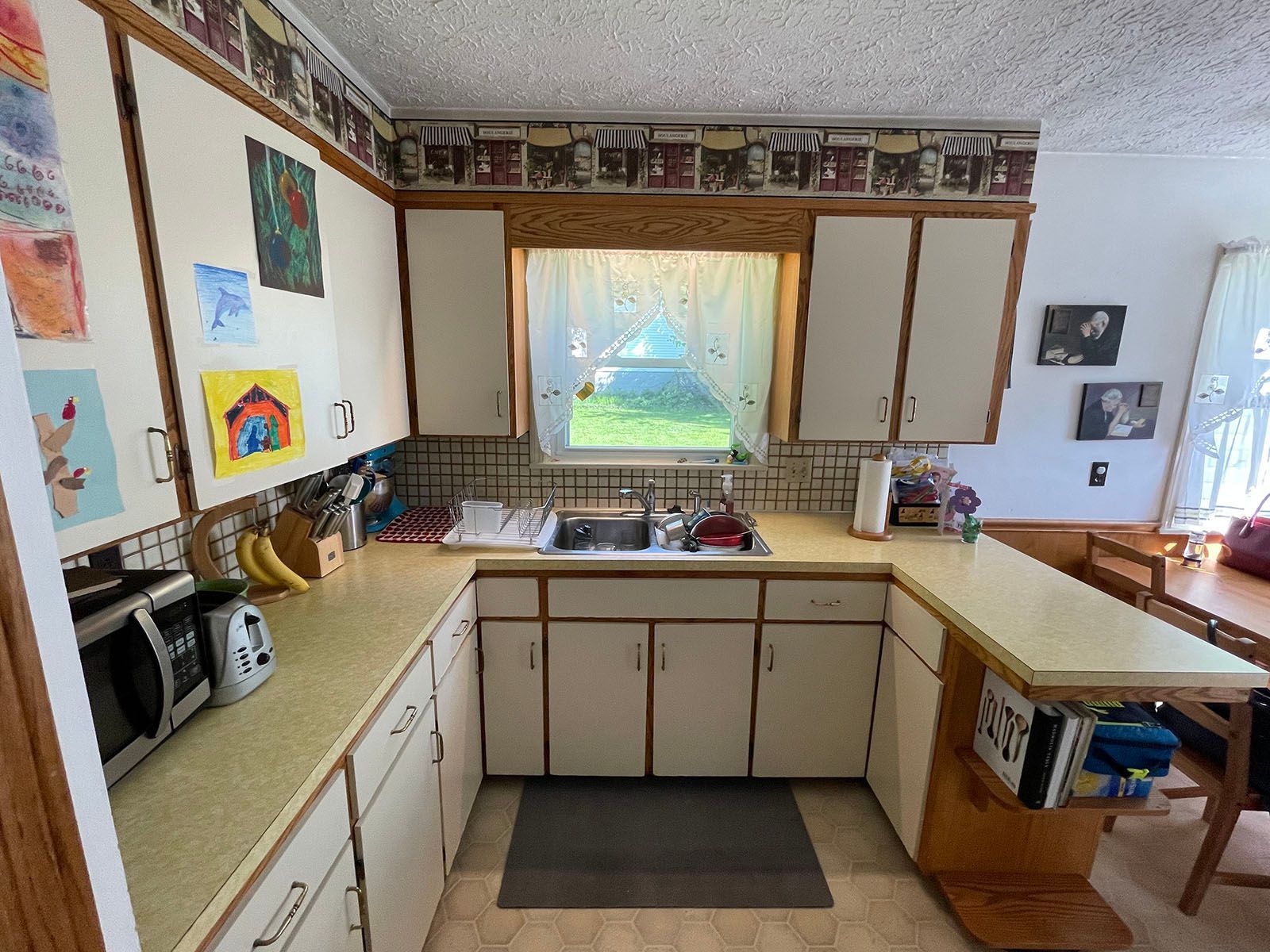 A kitchen with white cabinets , a sink , a microwave , and a window.