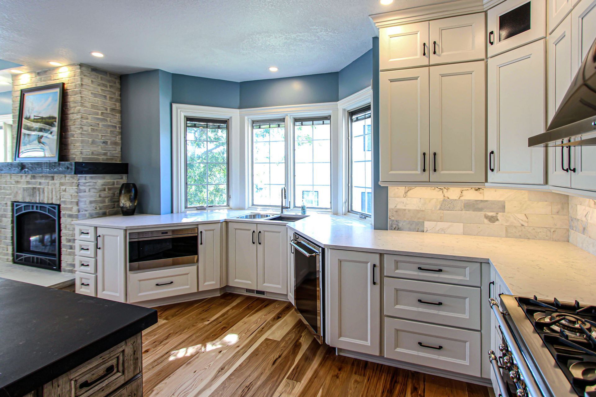 A kitchen with white cabinets , hardwood floors , stainless steel appliances and a fireplace.