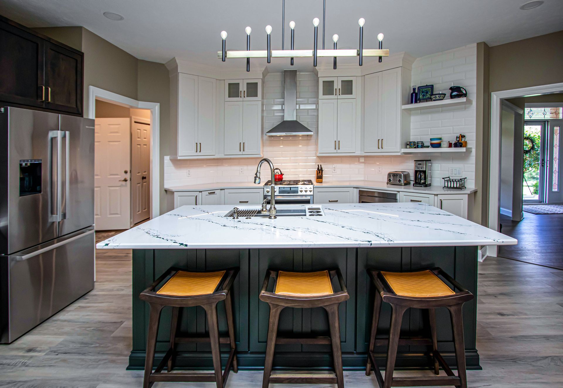 A kitchen with a large island , stools and a refrigerator.