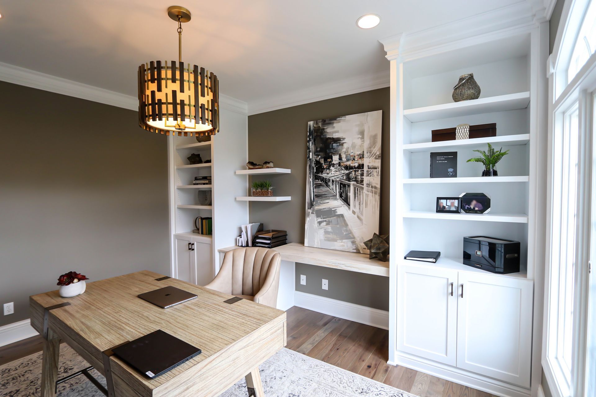 A home office with a desk , chair , shelves and a chandelier.
