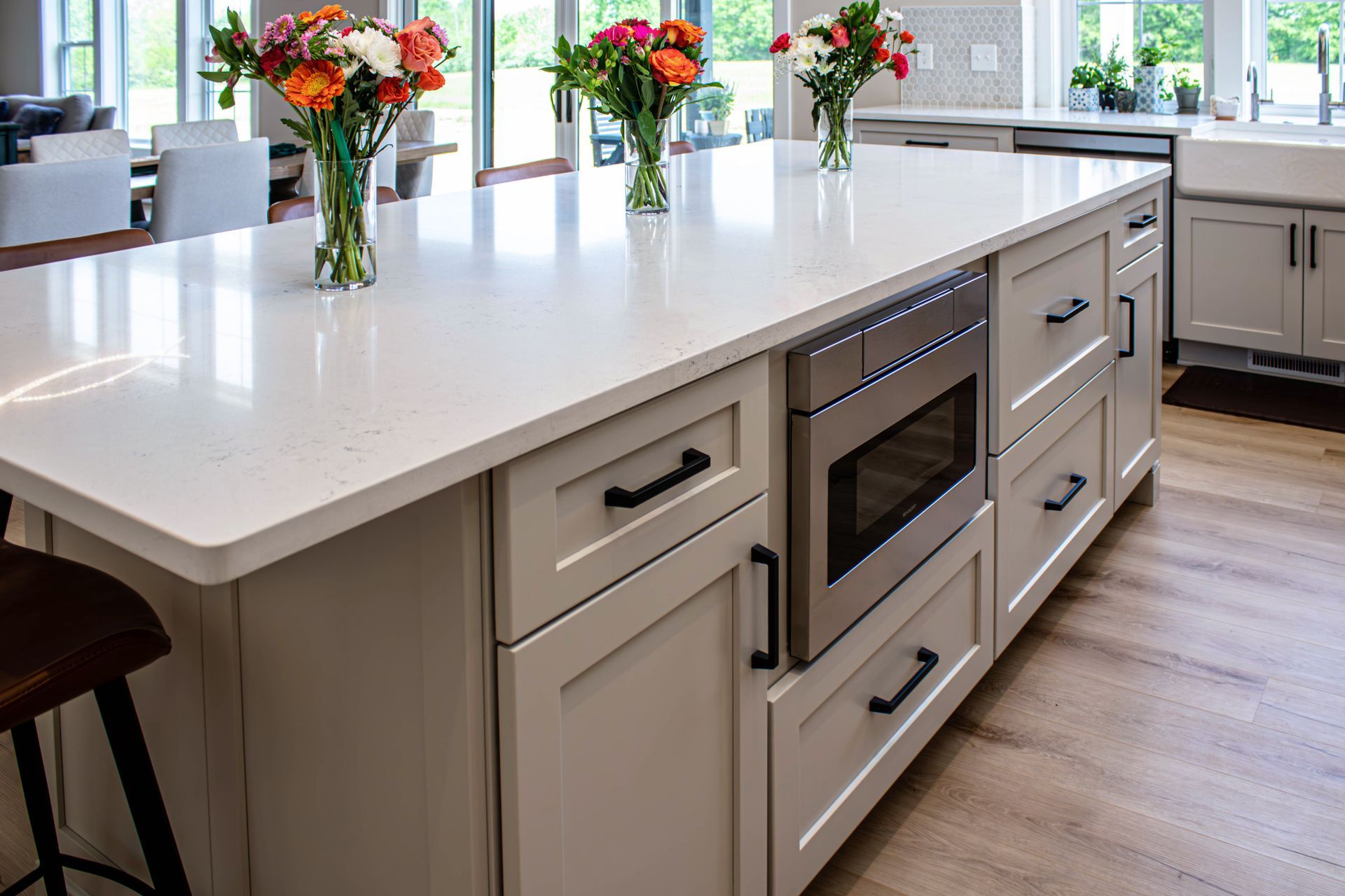 A kitchen with white cabinets , stainless steel appliances , and a large island with vases of flowers on it.