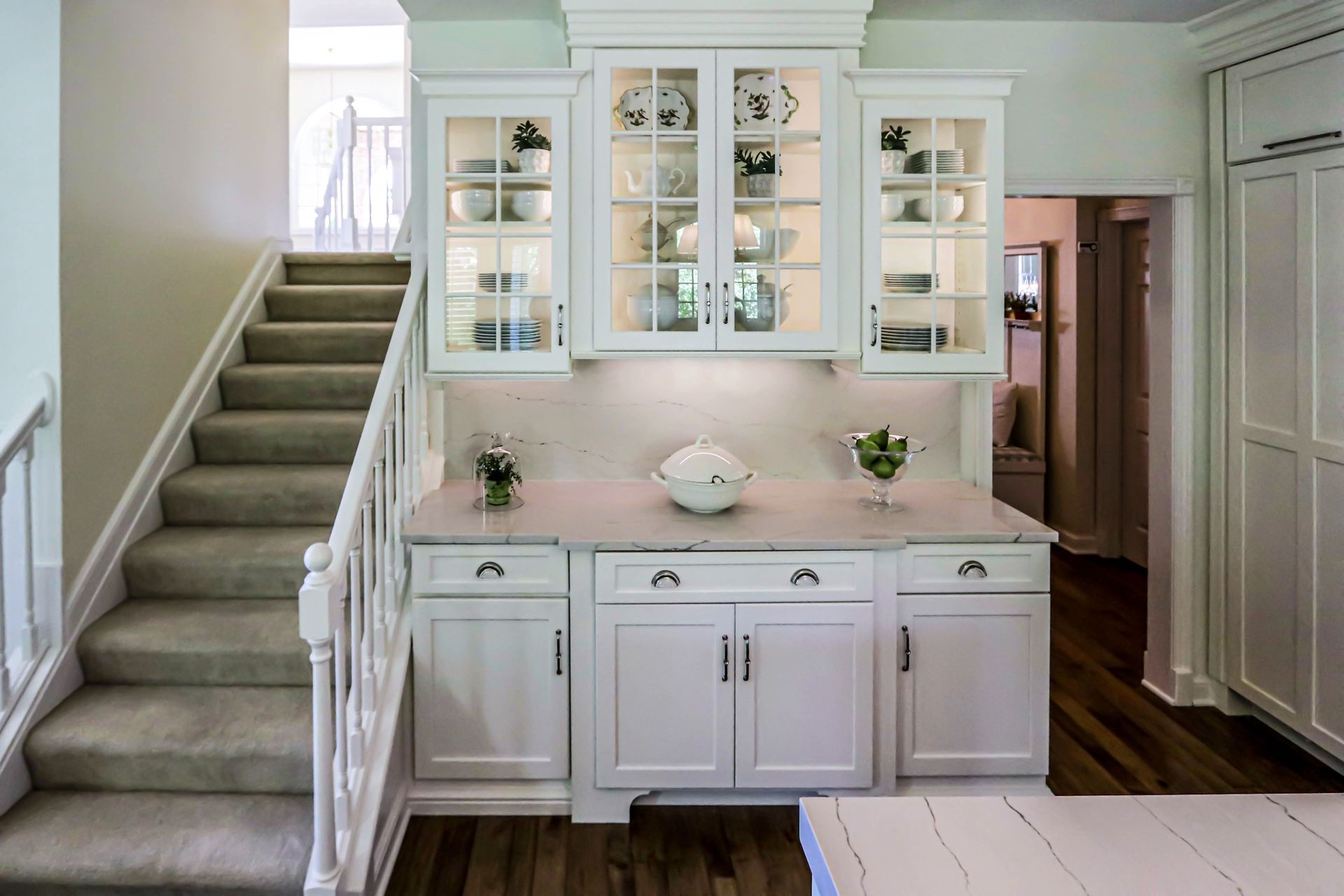 A kitchen with white cabinets and stairs leading up to it