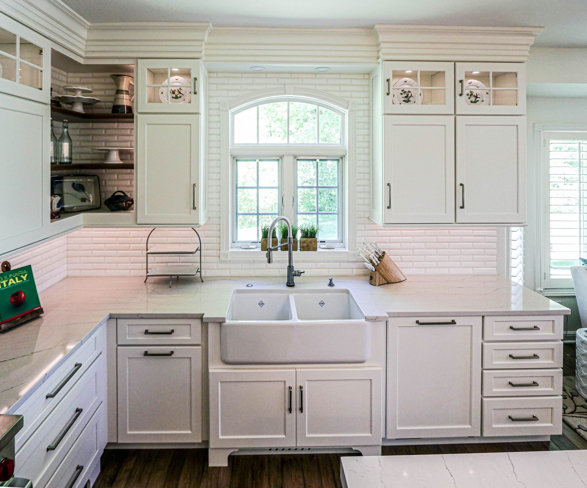 A kitchen with white cabinets , a sink , and a window.
