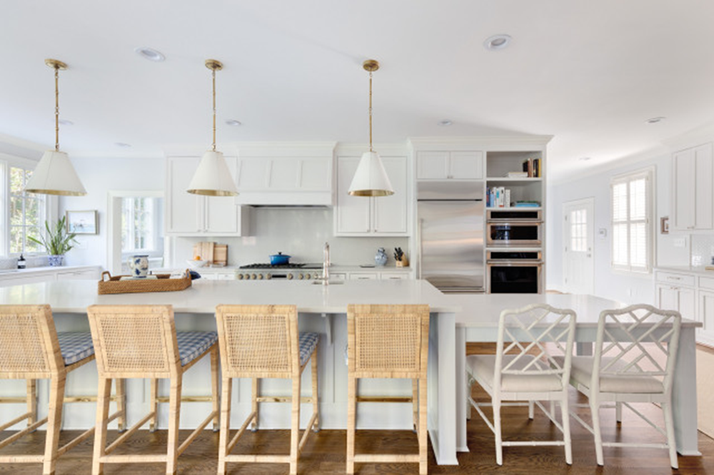 A kitchen with white cabinets , stainless steel appliances , and wicker chairs.