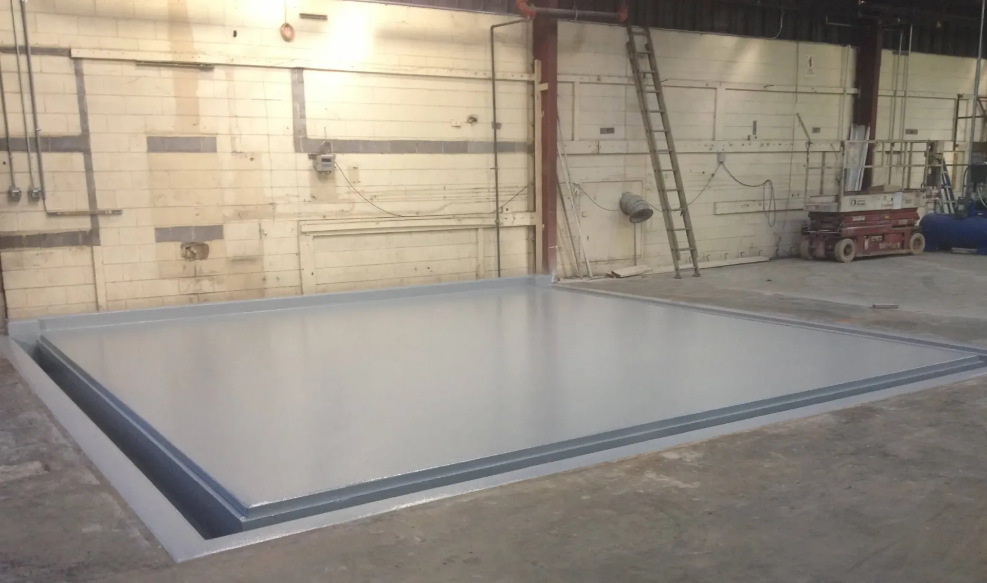 A large concrete floor in a warehouse with a ladder in the background.
