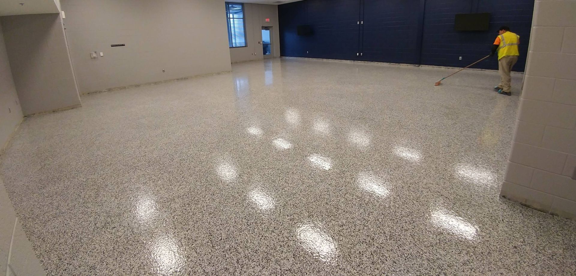 A man is sweeping the floor of a large room.