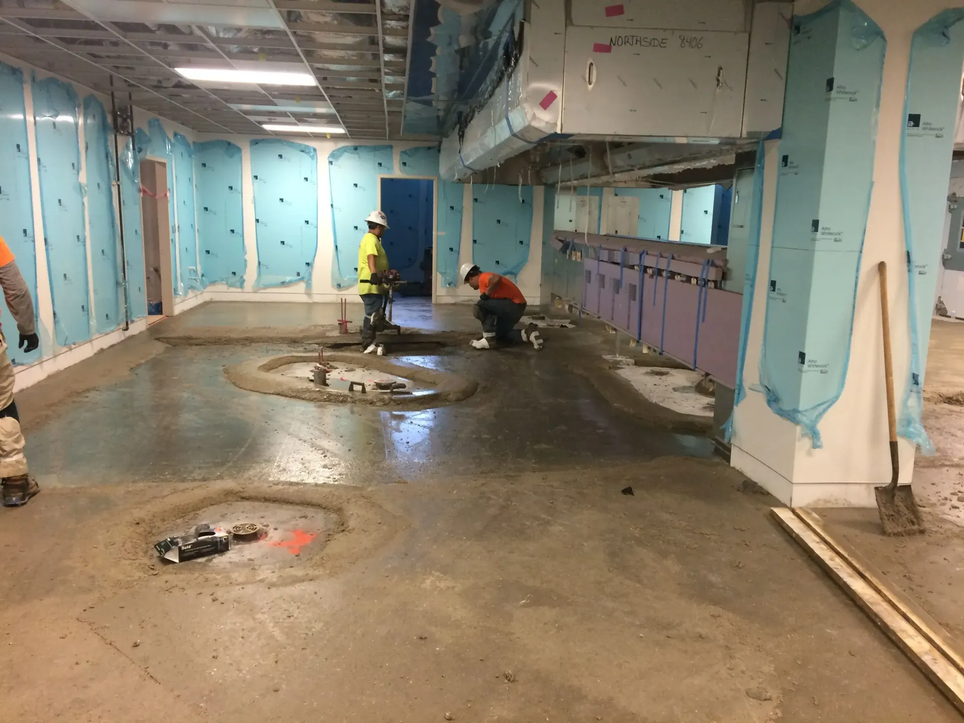 Two men are working on a concrete floor in a room.