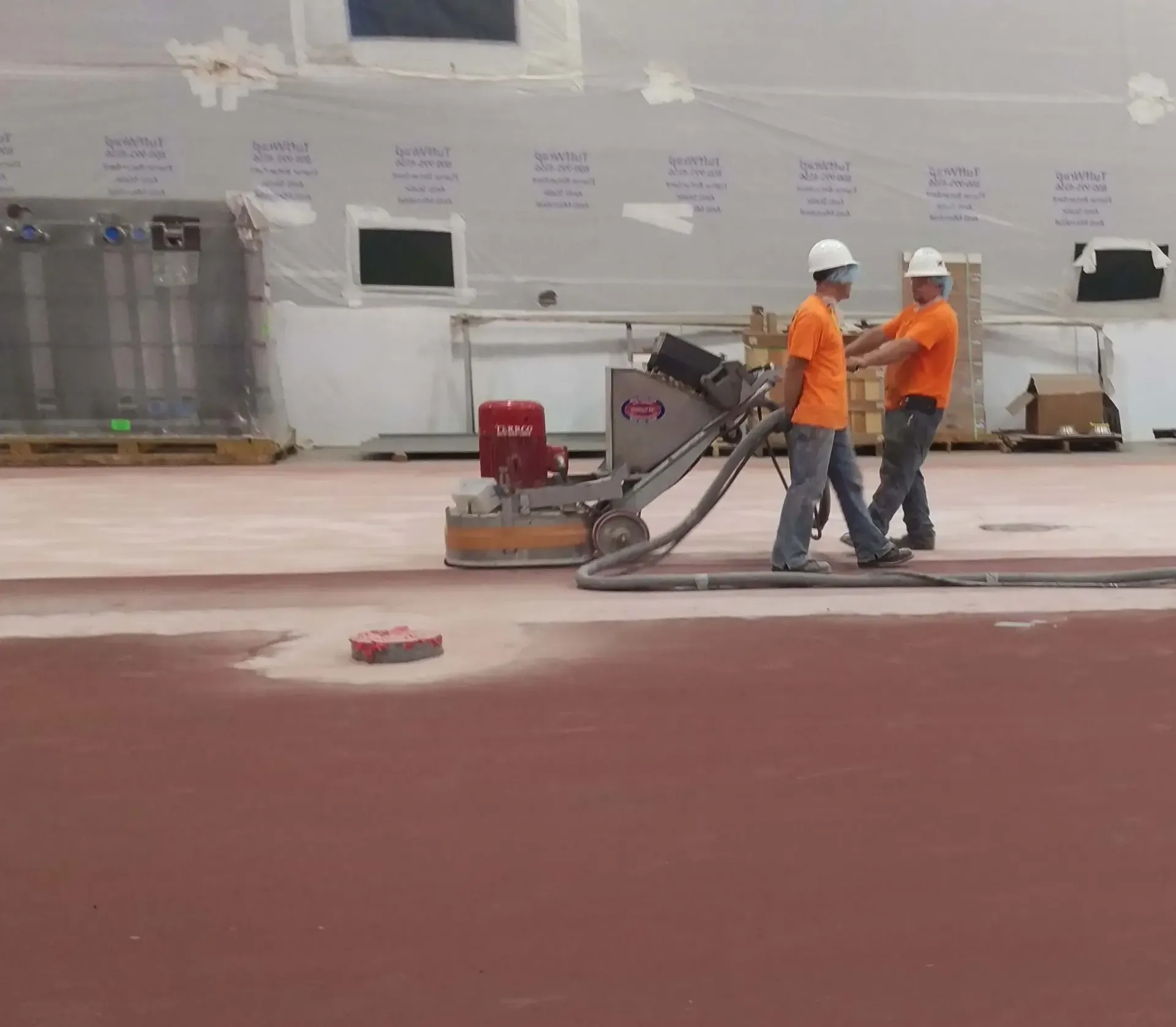 Two men wearing hard hats and orange shirts are working on a machine that says jmc on it