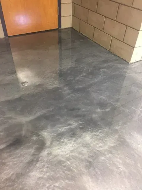 A gray metallic floor in a hallway next to a brick wall.