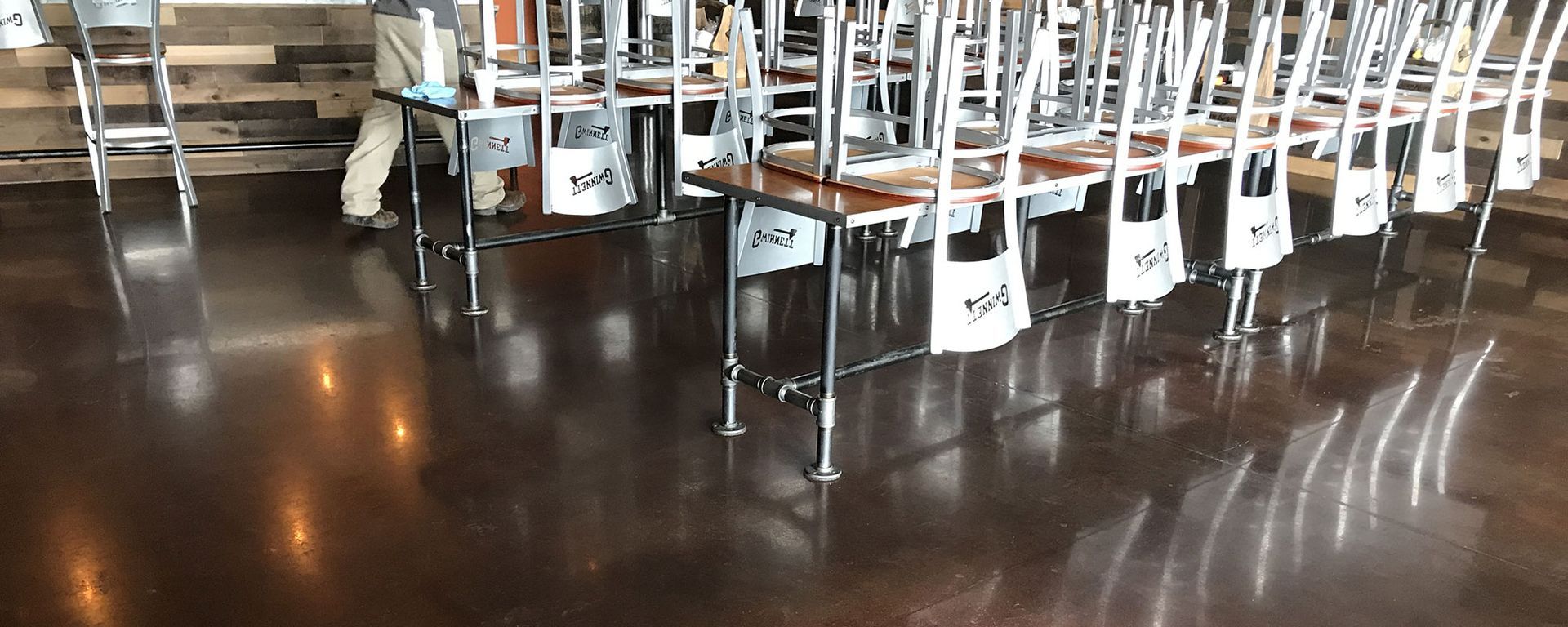 Tables with chairs up, on a dark, shiny floor. Neutral-toned walls in the background.