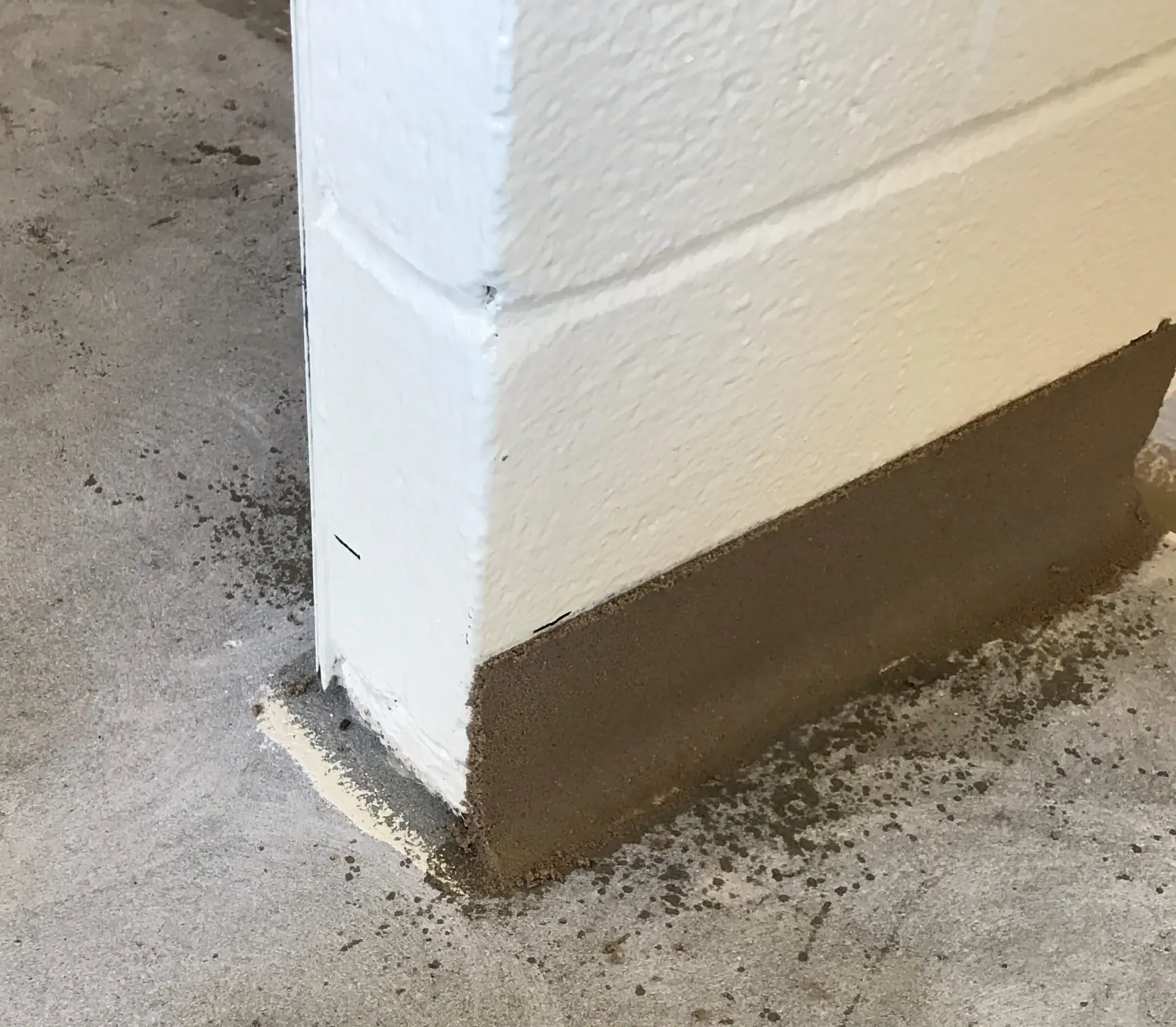 A white wall with a brown border is sitting on a concrete floor.