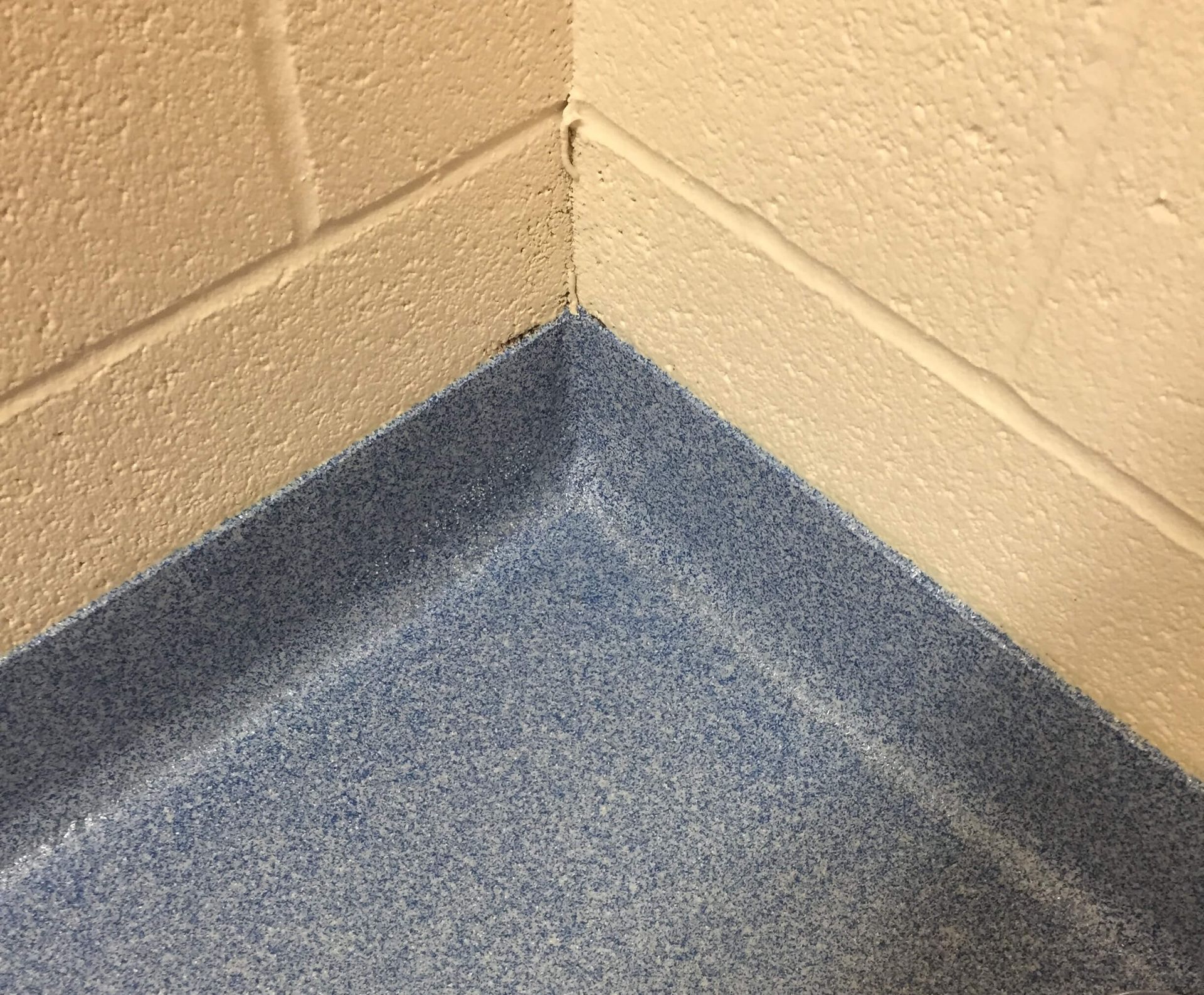 A corner of a room with a blue floor and a white brick wall.