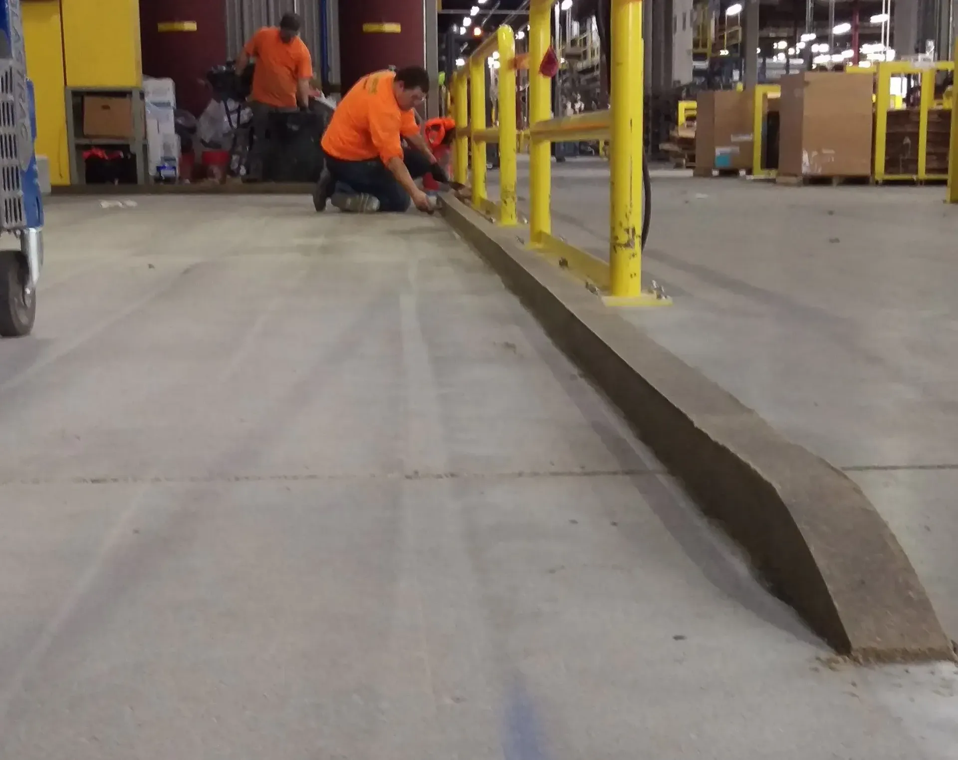 A man in an orange shirt is kneeling down in a warehouse