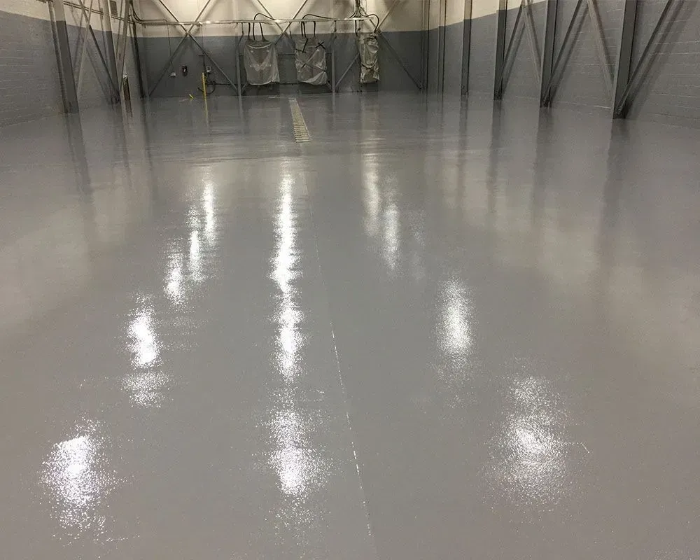 Gray industrial space with a glossy epoxy floor, reflecting the ceiling lights.