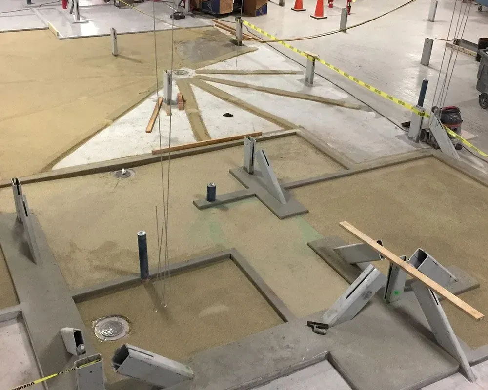Construction site with concrete forms, sand, and support structures on a large floor.