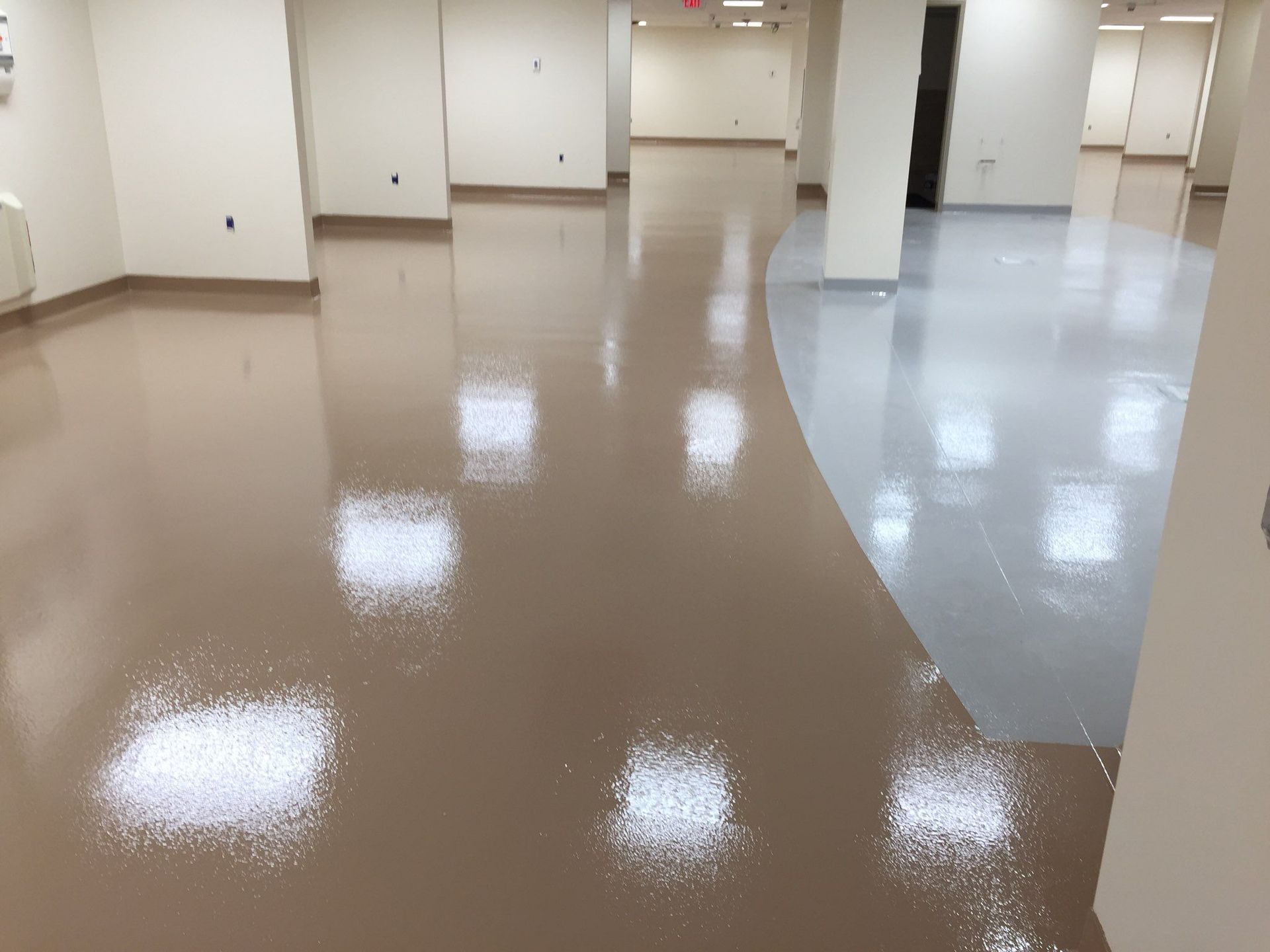 Brown and white glossy floor in a building hallway, reflecting overhead lights.