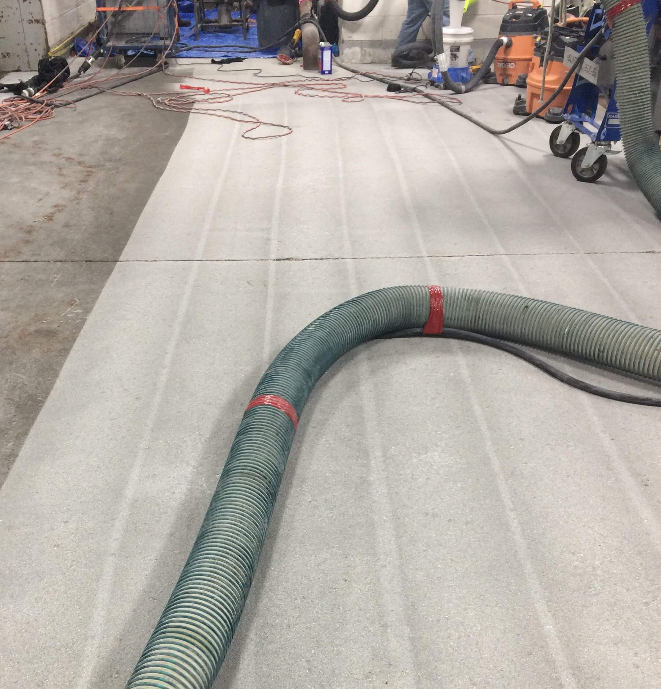 A green hose is laying on the floor next to a vacuum cleaner