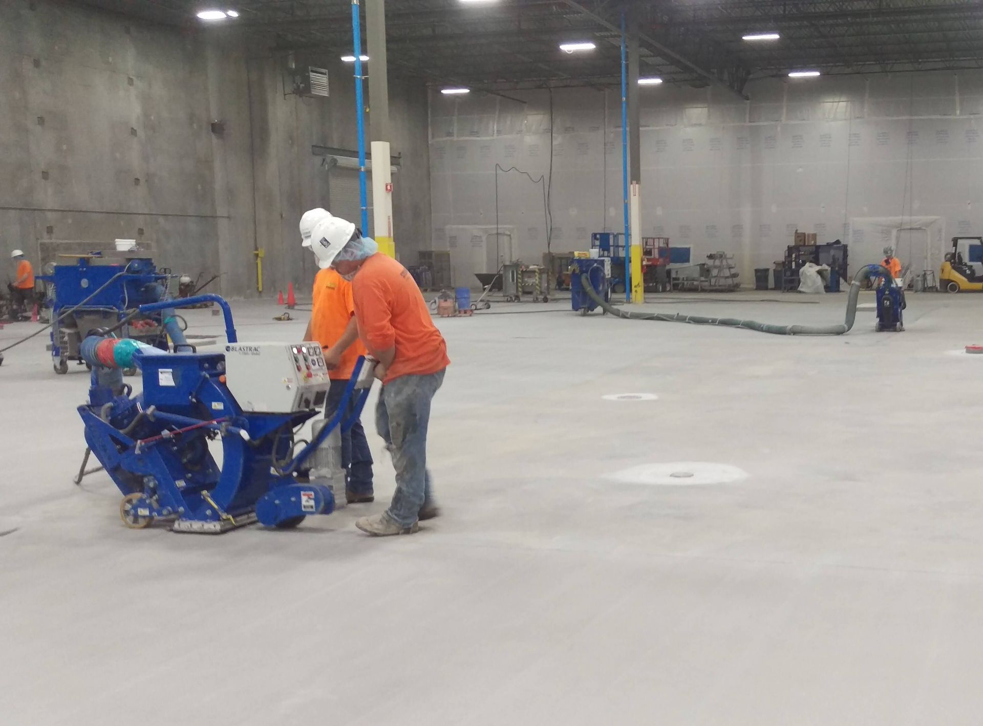 Two men are working on a concrete floor in a large warehouse.
