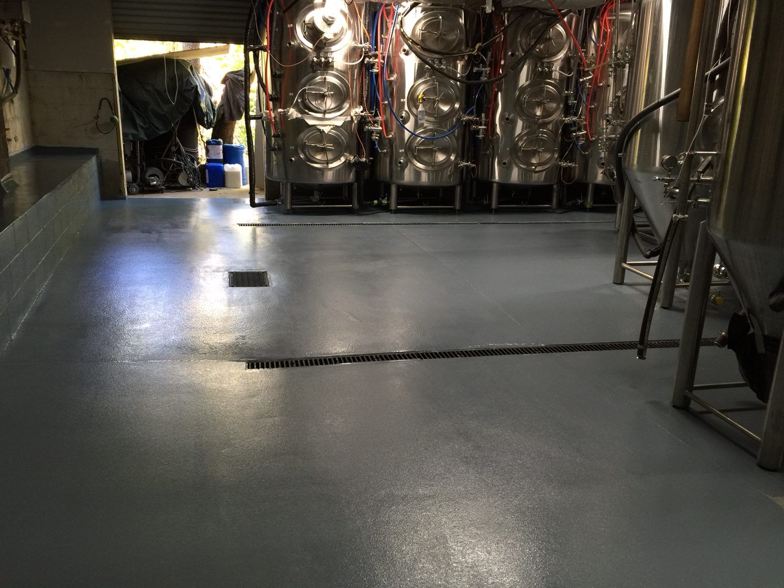 Light blue industrial floor in brewery with stainless steel tanks.