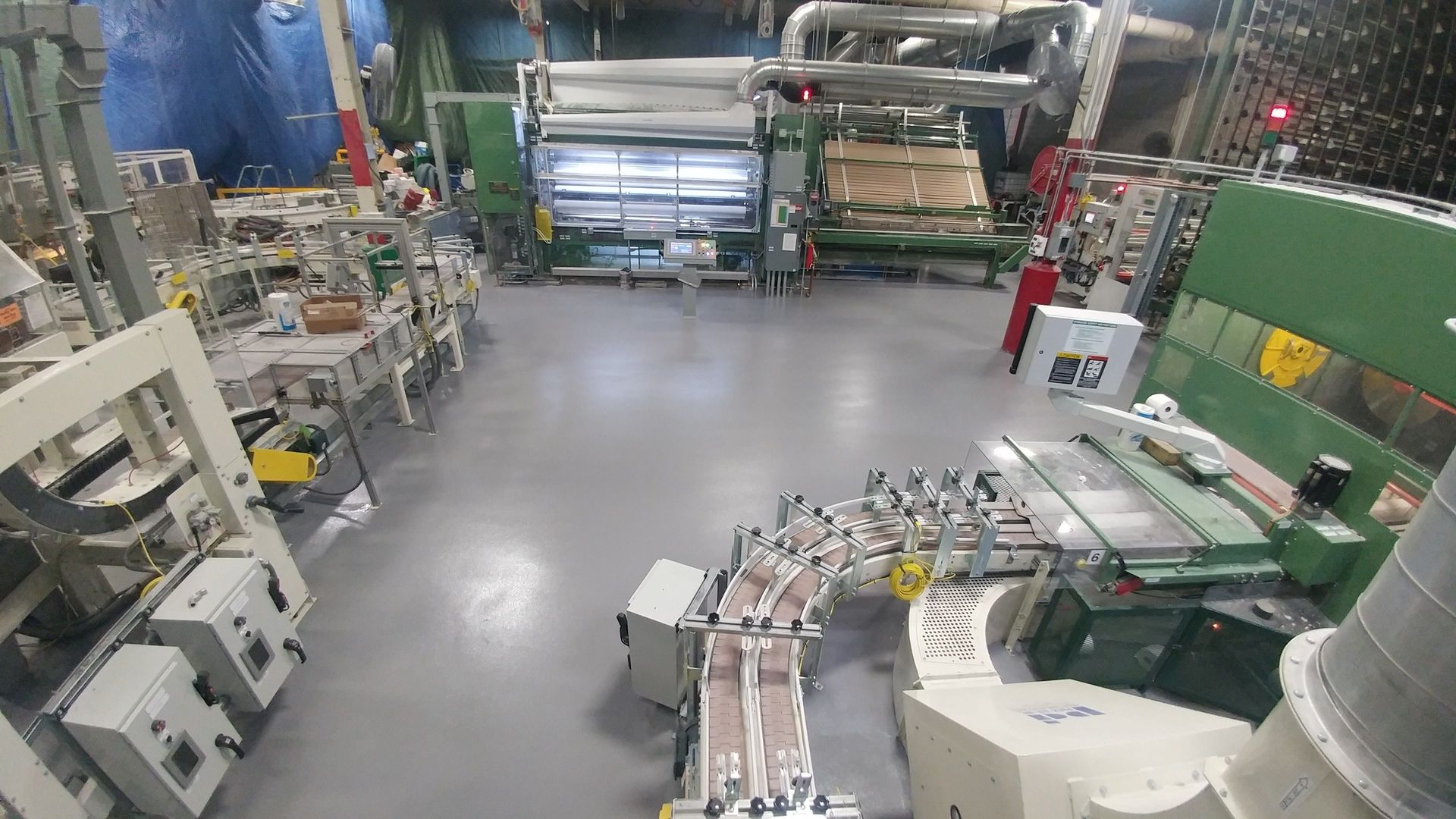A factory interior with machines, conveyor belts, and equipment; mostly grey and green.