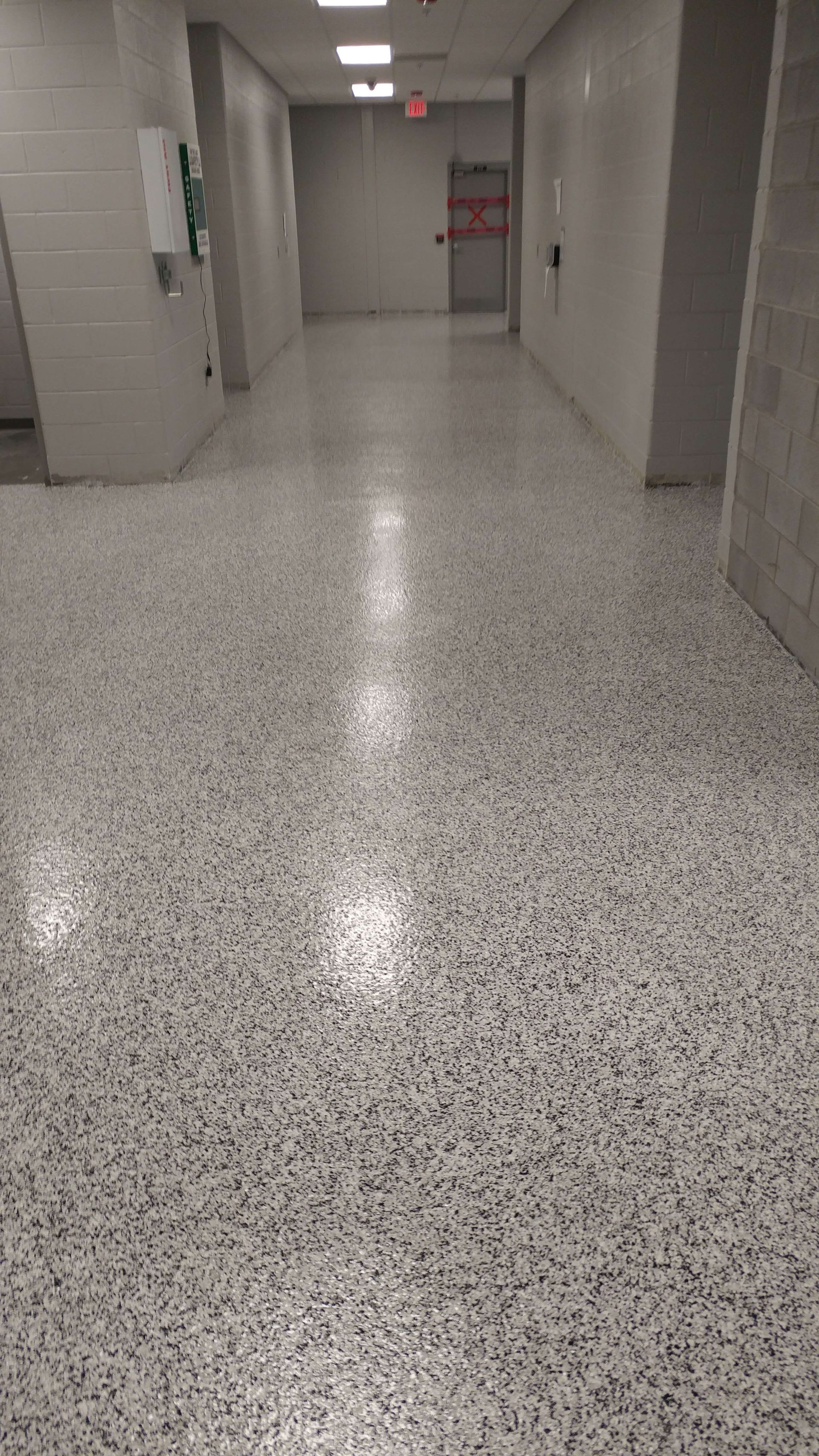 A long hallway with a white tiled floor and a red exit sign.